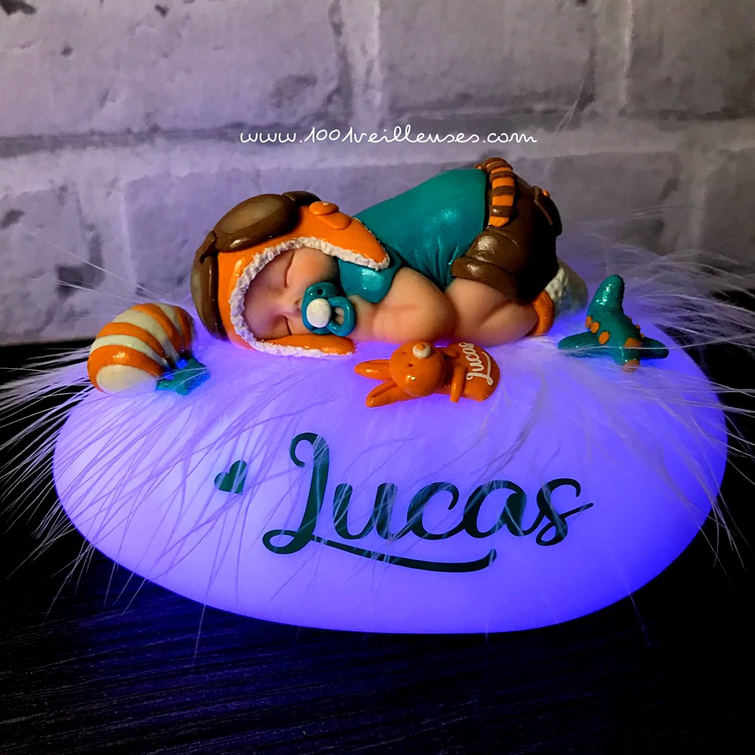 Luz nocturna personalizada en forma de guijarro luminoso con un bebé de fimo disfrazado de aviador junto a una caja de regalo