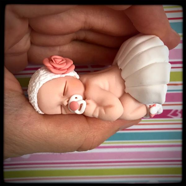 Habillage du bébé en fimo avec une robe et un bandeau tenu dans la main