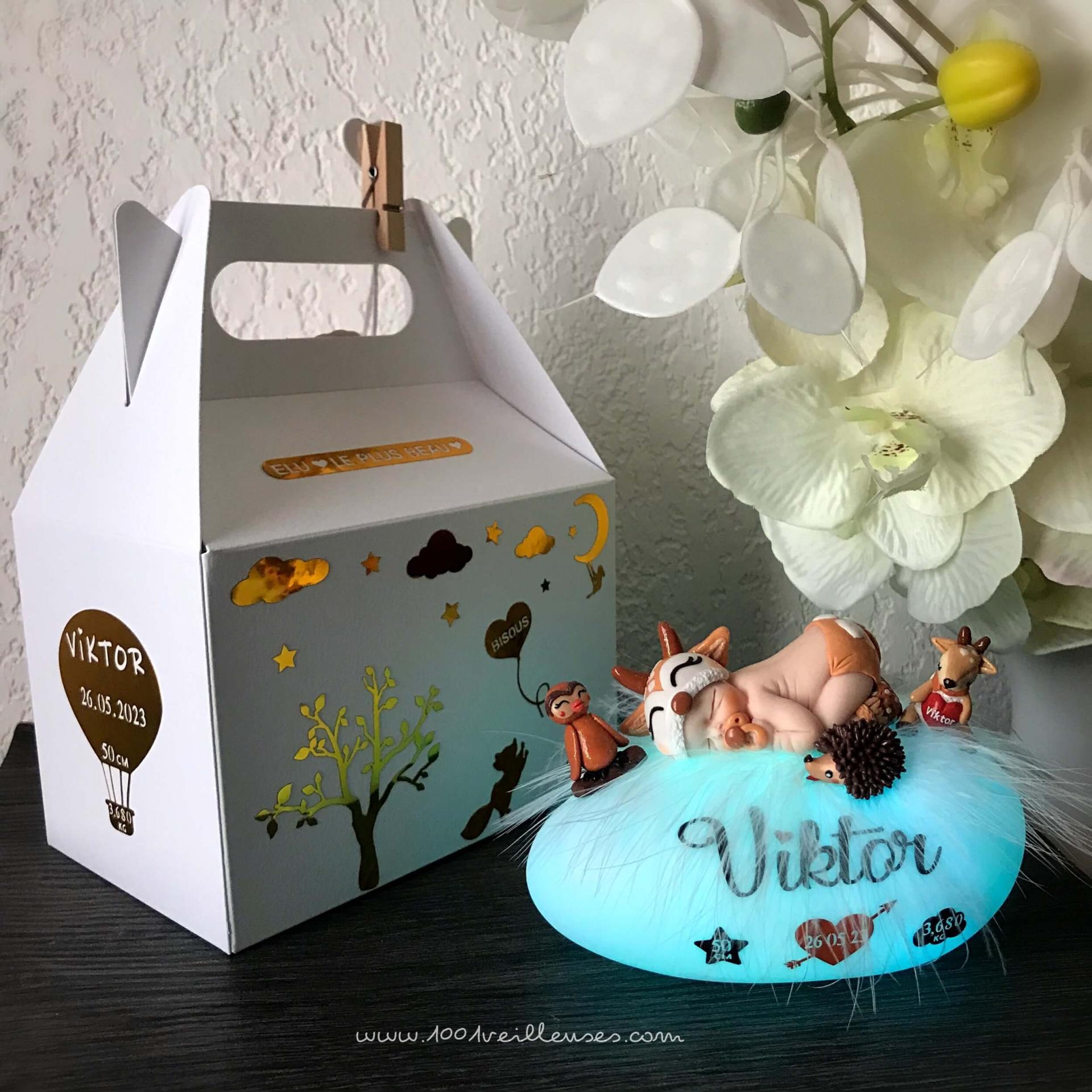 Back view of the personalized night light with a baby sculpted in fimo dressed as a fawn, next to its matching personalized gift box, illuminated night light