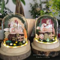 Two babies (white and gray) under LED bells in a glass dome miniature setting