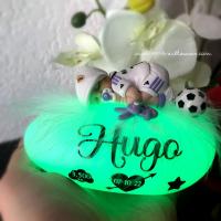 Lámpara de noche personalizada en forma de guijarro luminoso con un bebé de fimo vestido como un jugador de fútbol del Real Madrid, junto a una caja de regalo