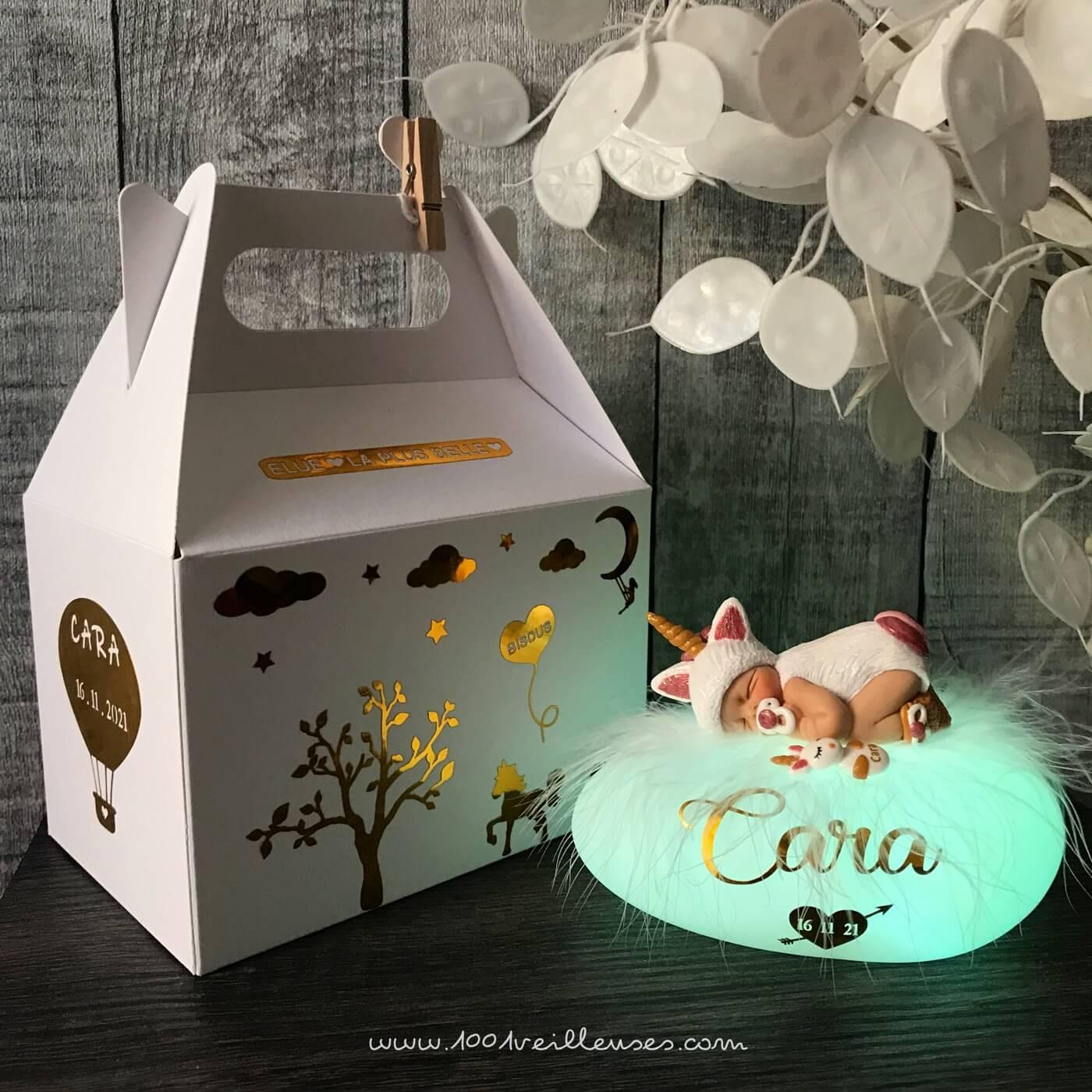 Customized night light in the shape of a glowing pebble with a baby girl dressed as a unicorn, accompanied by a gift box