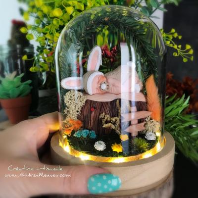 Magnifique veilleuse artisanale allumée sous forme de dôme en verre avec un jardin miniature sur le thème du lapin, présentée à côté d'une main